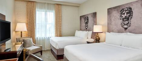 A hotel room with two beds, a desk with a chair, a TV, and artwork on the walls.