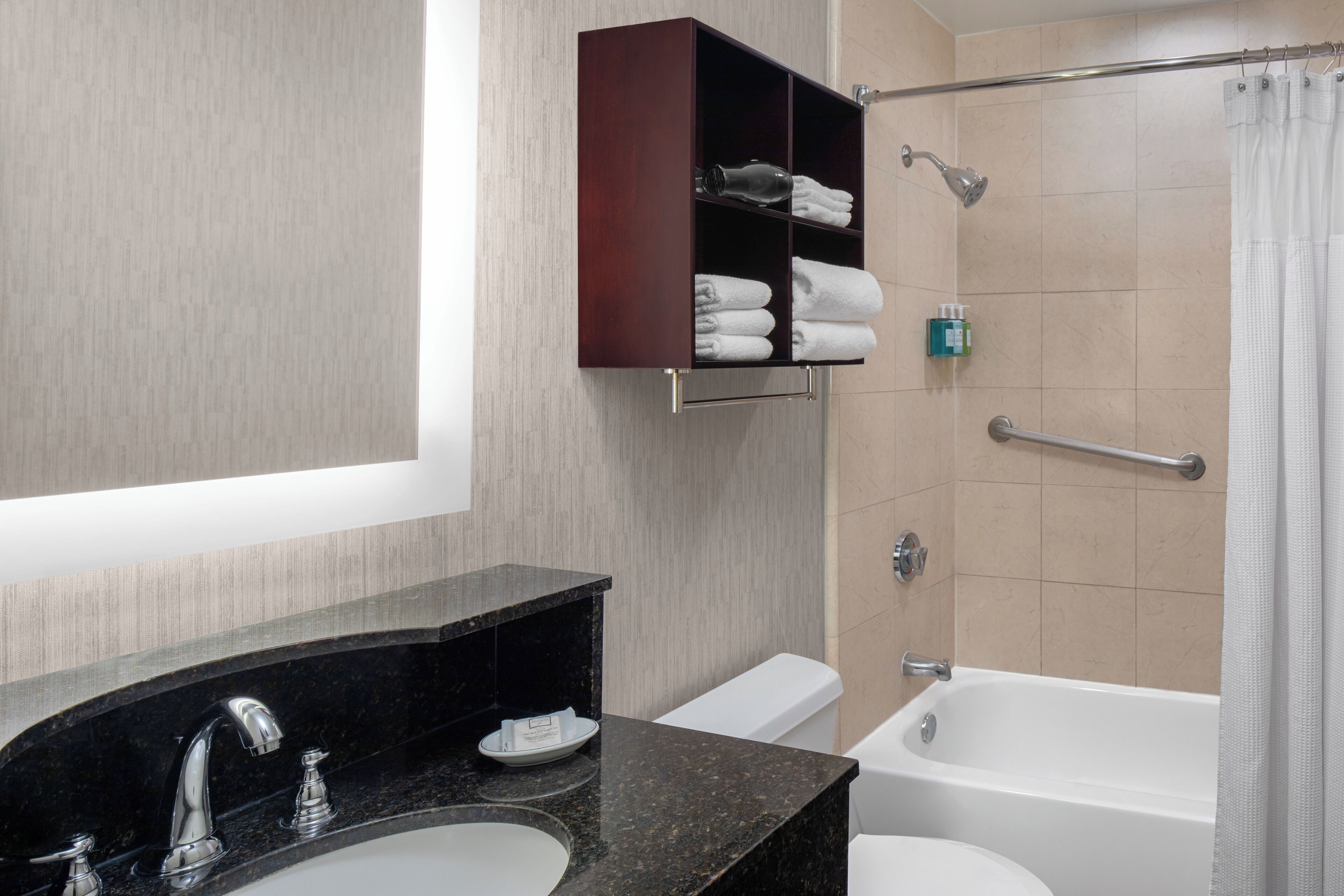 A bathroom with a black marble sink, a white toilet, a shower with a glass door, and a dark wooden cabinet above the sink.