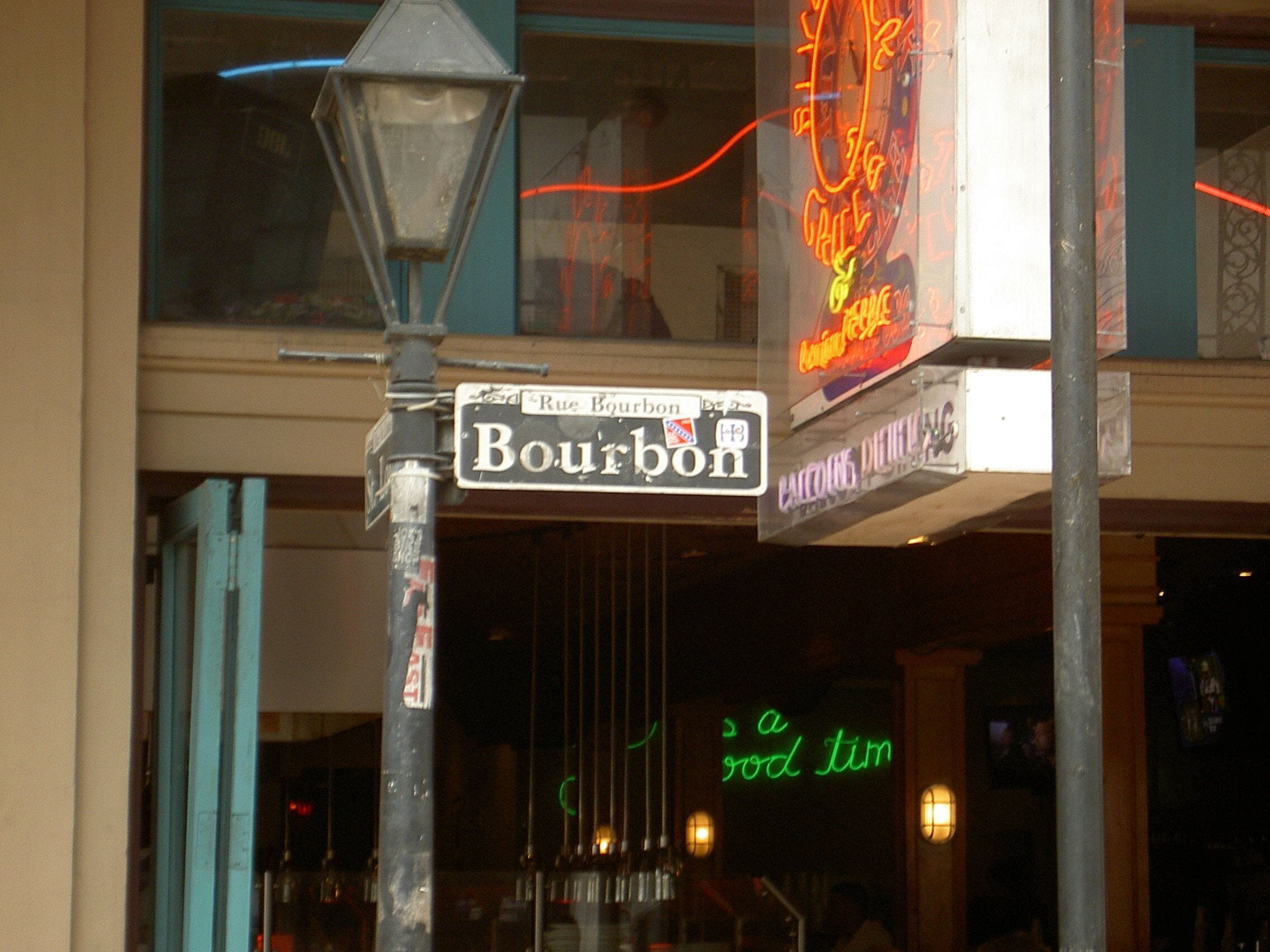 Un panneau de rue indiquant « Bourbon Street », avec une enseigne au néon en arrière-plan.