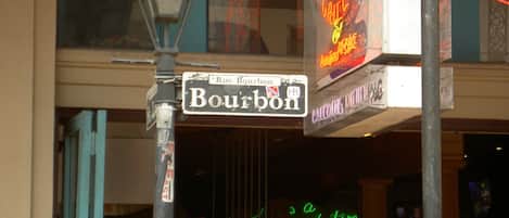 Una señal de calle indica Bourbon Street, con un letrero de neón al fondo.