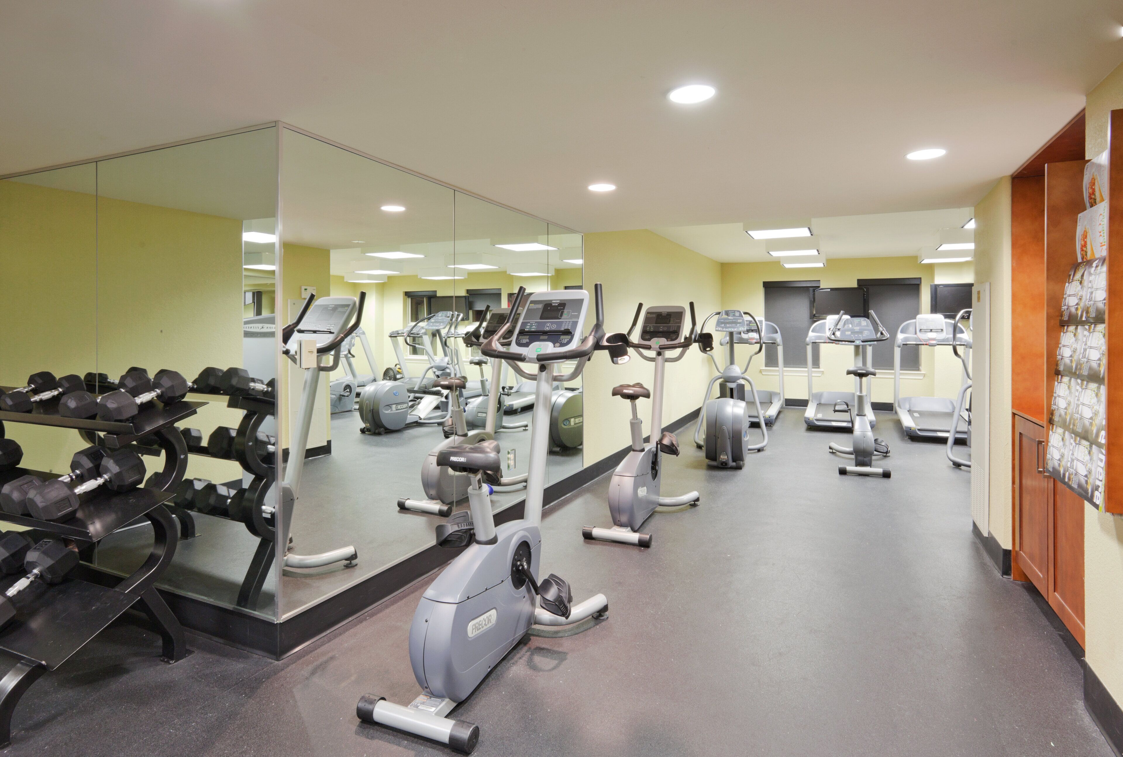 Ein Fitnessstudio mit verschiedenen Trainingsgeräten, darunter Laufbändern und Kurzhanteln, und einem großen Spiegel, der den Raum widerspiegelt.