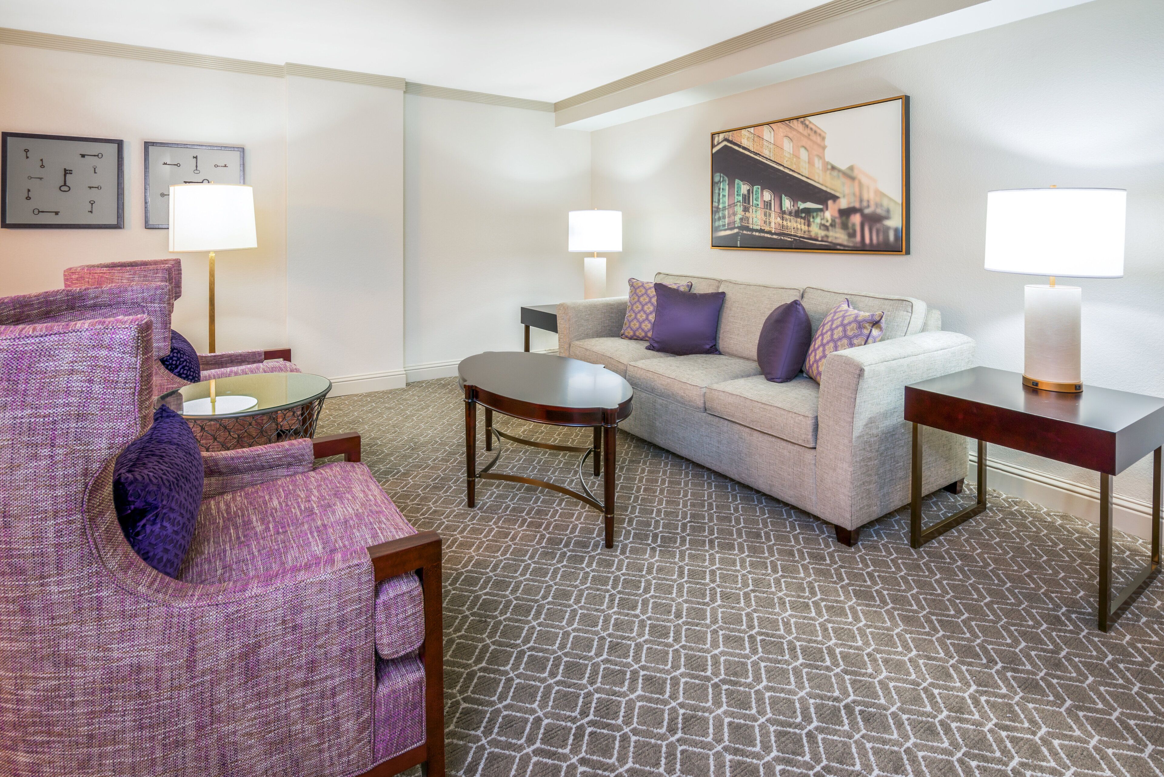 A hotel room with a patterned carpet, a sofa, a chair, a small round table, and two lamps.