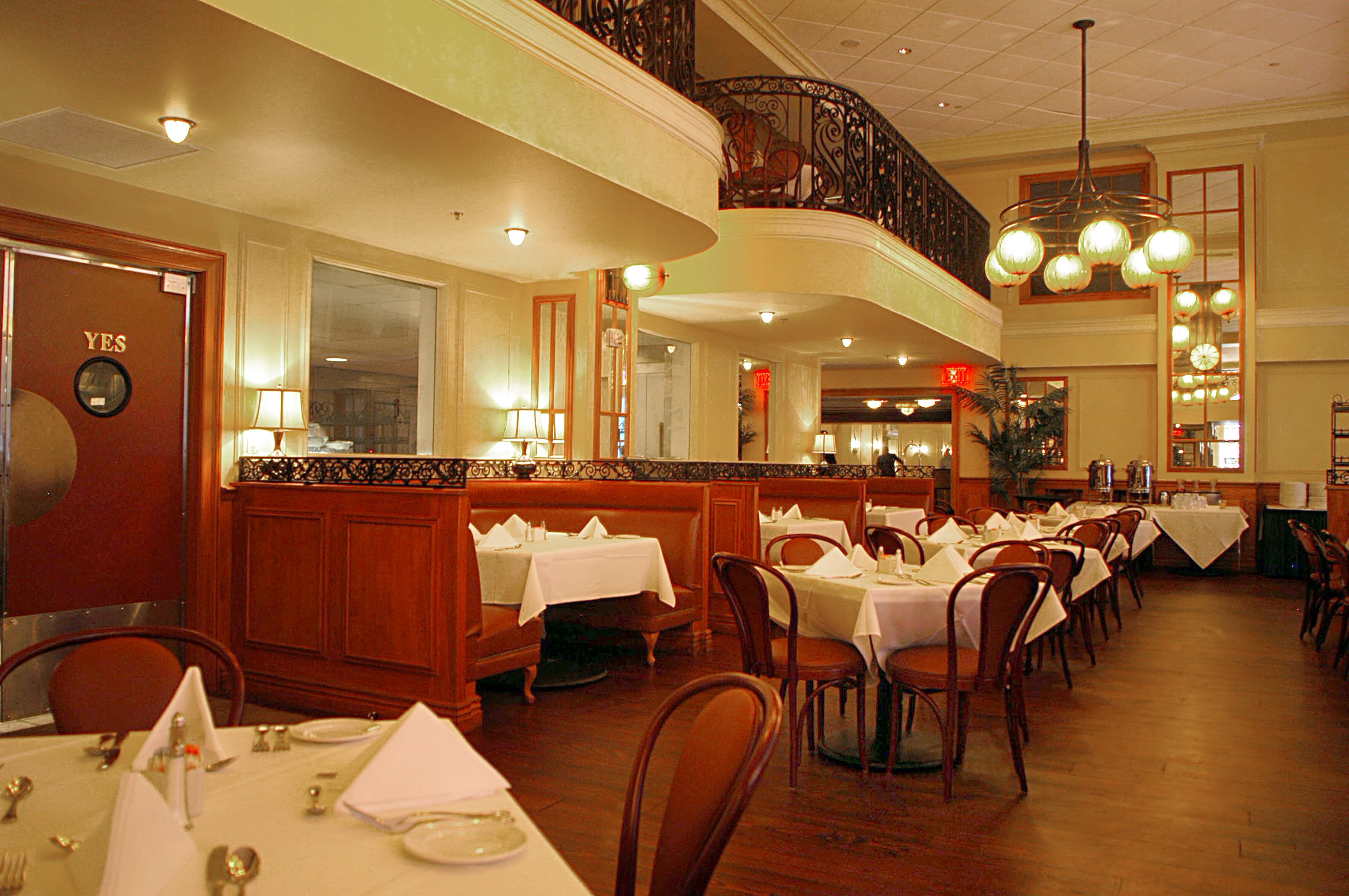 A restaurant with multiple dining tables and booths, a balcony with ornate railings, and a chandelier.