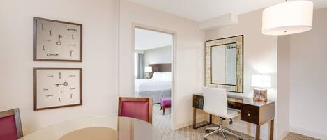 A hotel room with a round glass table, a desk with a chair, a large mirror, and two framed key collections on the wall.