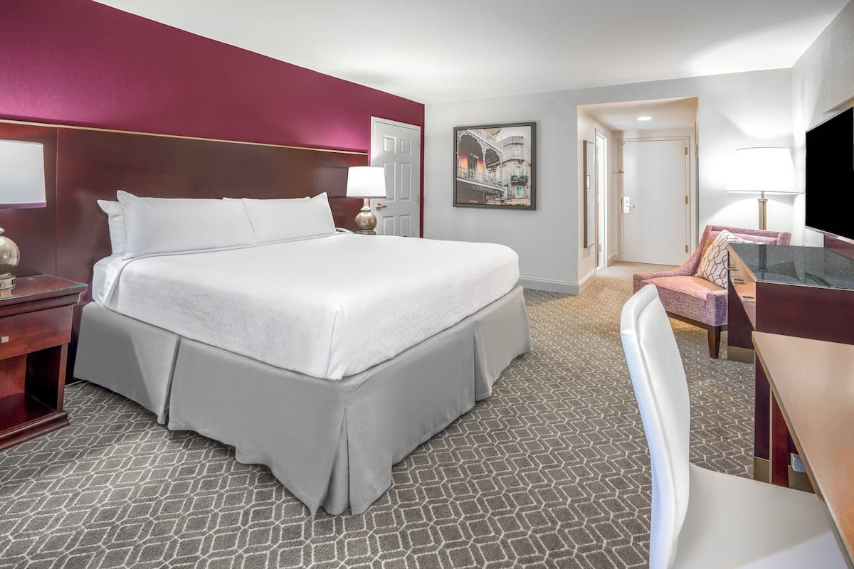 Ein Hotelzimmer mit einem großen Bett, einem Schreibtisch, einem Sessel, einem Fernseher und einer Tür zu einem weiteren Raum.