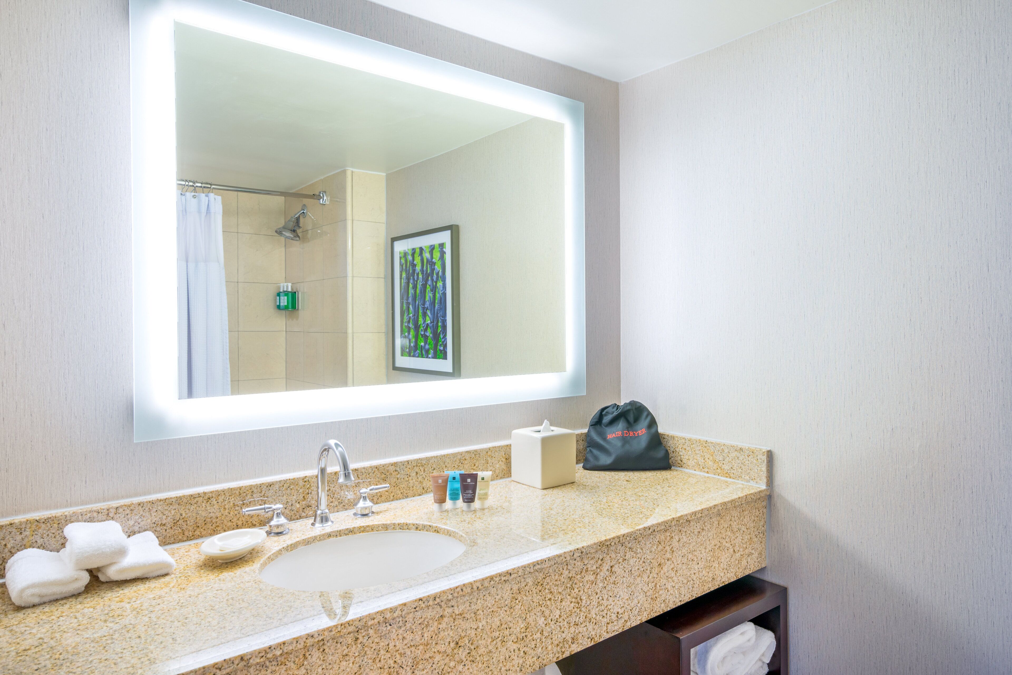 Un baño con un espejo grande, lavamanos y perchero para toallas.