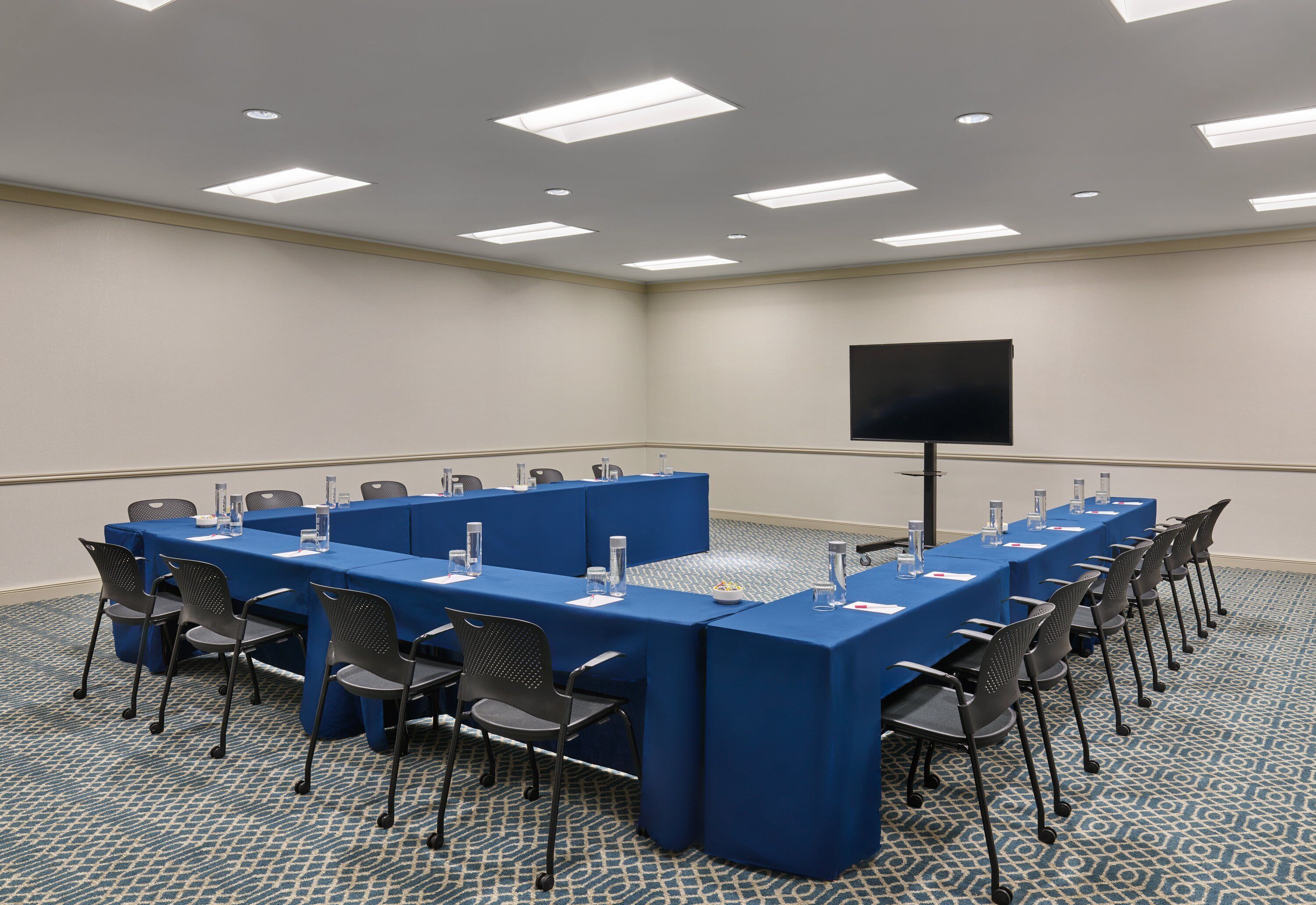 A conference room with a long table, chairs, a screen, and a carpeted floor.