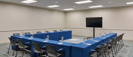 A conference room with a long table, chairs, a screen, and a carpeted floor.