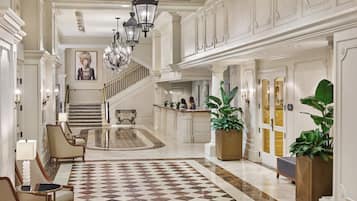 Un vestíbulo amplio con piso a cuadros, una mesa de recepción y una escalera que sube a los pisos superiores.