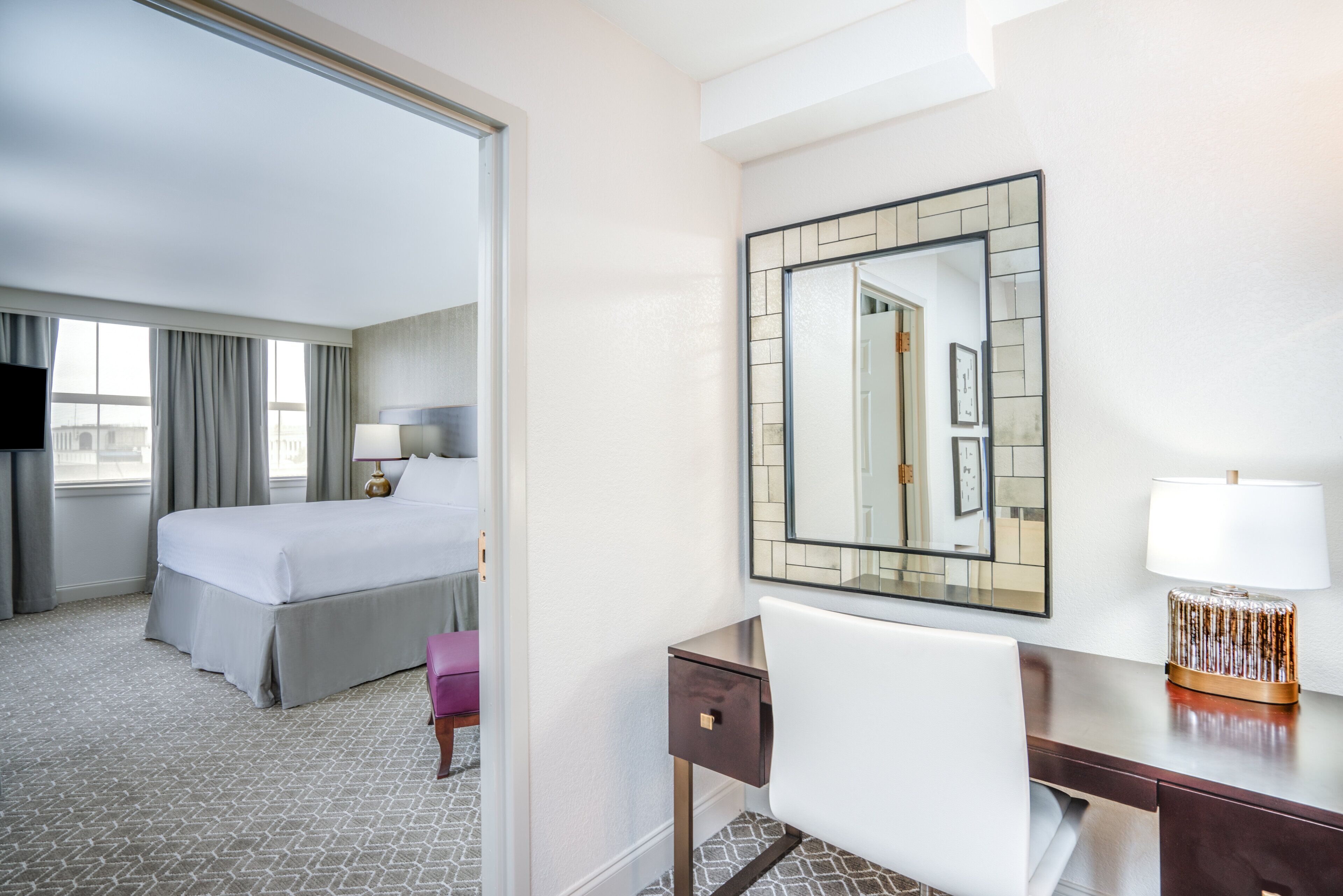 Ein Hotelzimmer mit einem Bett, einem Schreibtisch, einem Sessel, einer Lampe und einem großen Spiegel.
