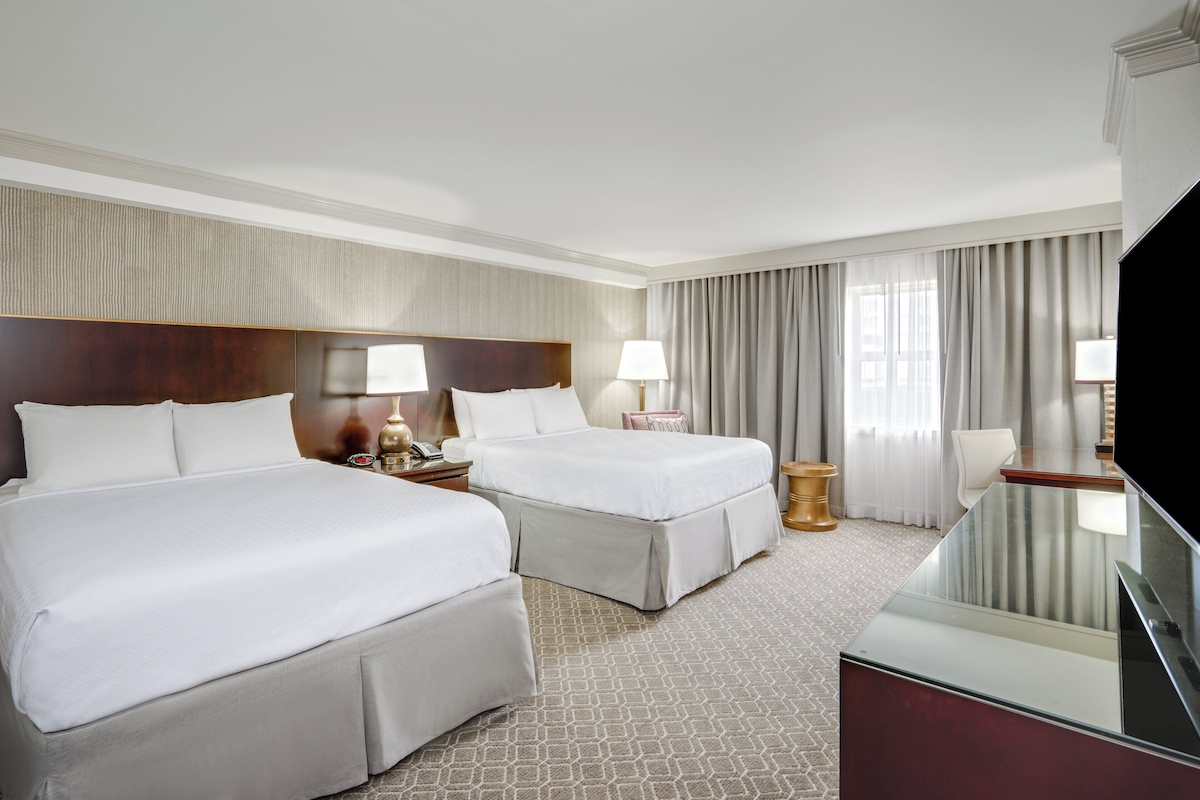 Ein Hotelzimmer mit zwei Betten, einem Fernseher, einem Schreibtisch und einem Badezimmer.