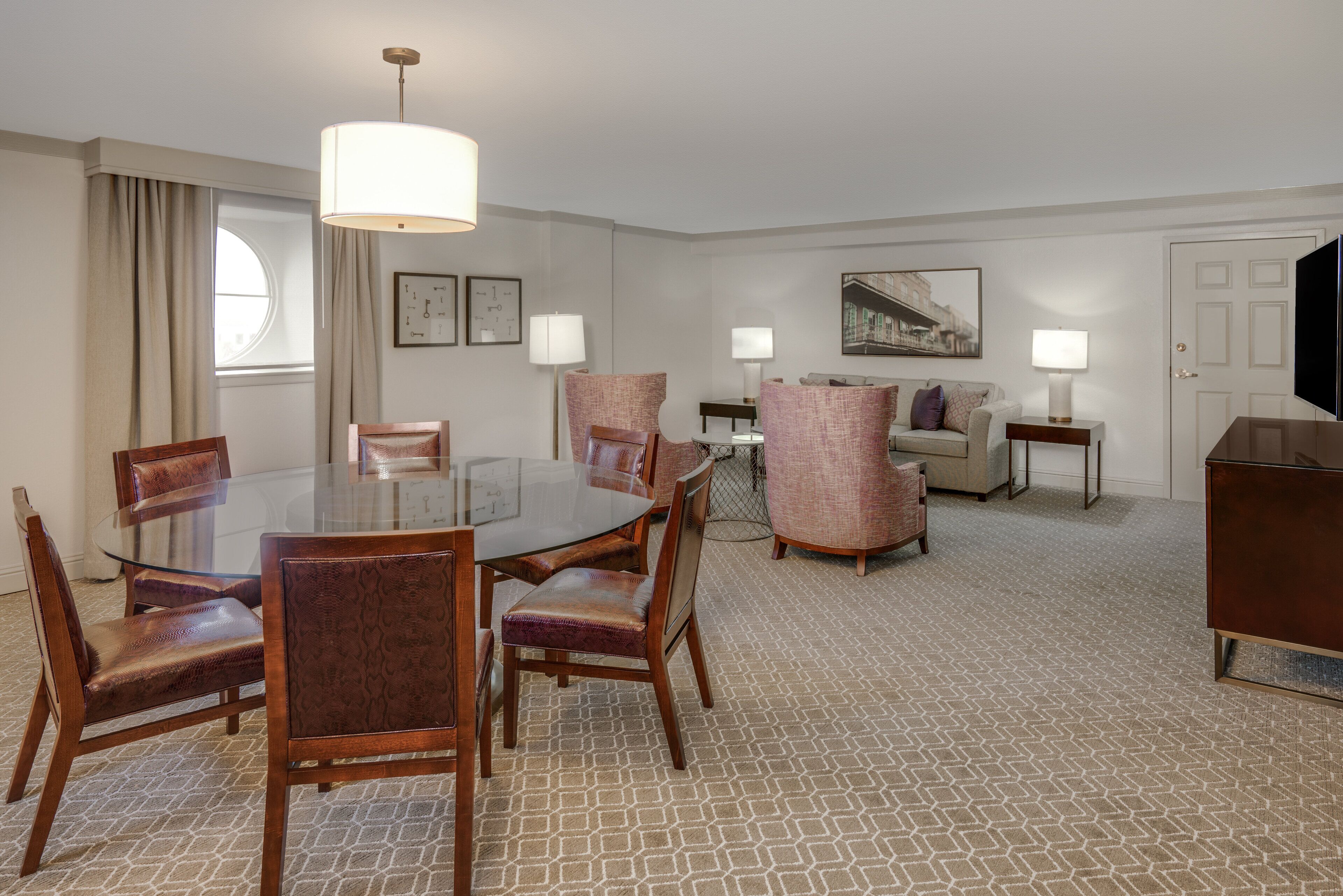 Habitación de hotel con comedor, sofá, televisor y un cuadro en la pared.