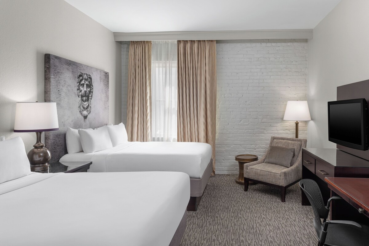 Een hotelkamer met twee bedden, een televisie, een stoel en een lamp.