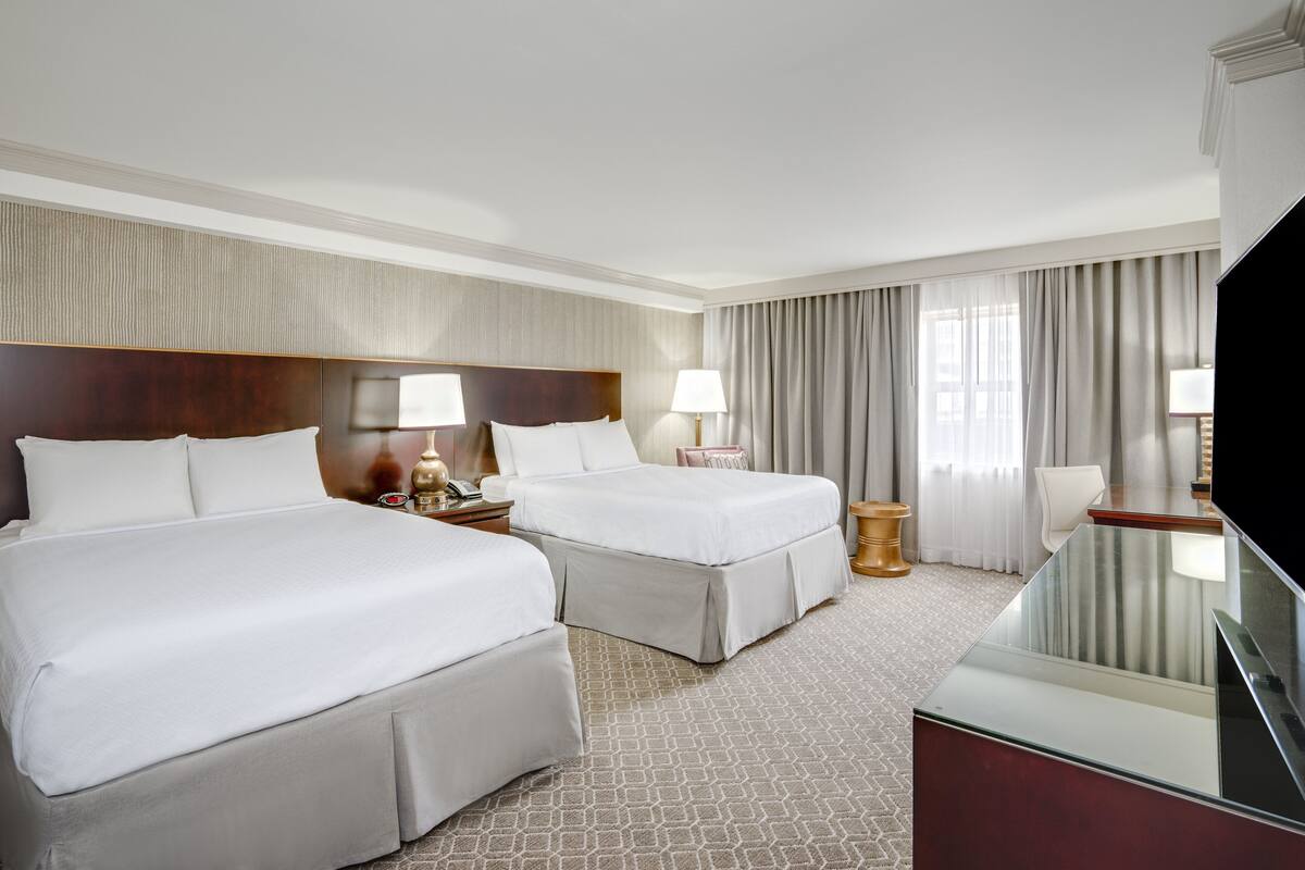 Quarto de hotel com duas camas, televisão, escrivaninha e banheiro.
