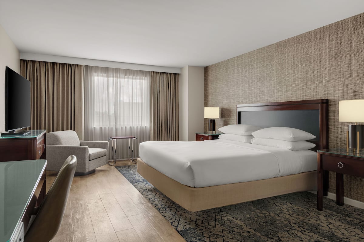Une chambre d’hôtel avec un grand lit, un bureau, une chaise, une télévision et une fenêtre avec des rideaux.