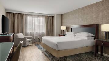 Une chambre d’hôtel avec un grand lit, un bureau, une chaise, une télévision et une fenêtre avec des rideaux.