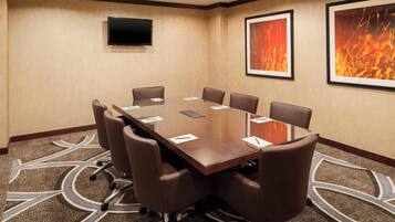 A conference room with a large table, eight chairs, a flat-screen TV, and framed artwork on the walls.