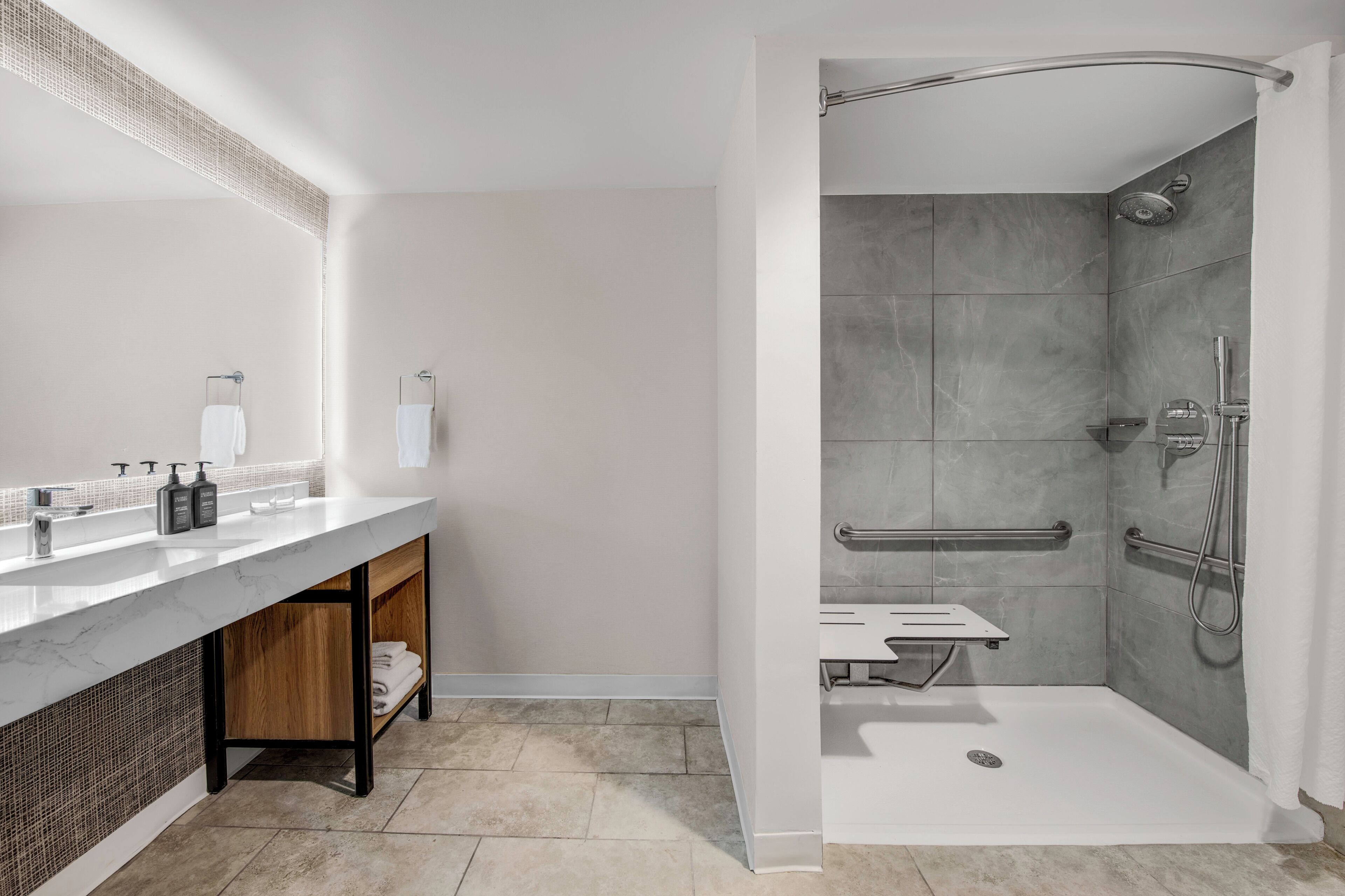 Une salle de bain moderne avec un meuble-lavabo en marbre, une douche équipée de barres d’appui et un lavabo blanc.