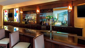 Zona de bar con distintas opciones de asientos, una variedad de botellas y una pantalla de televisión.