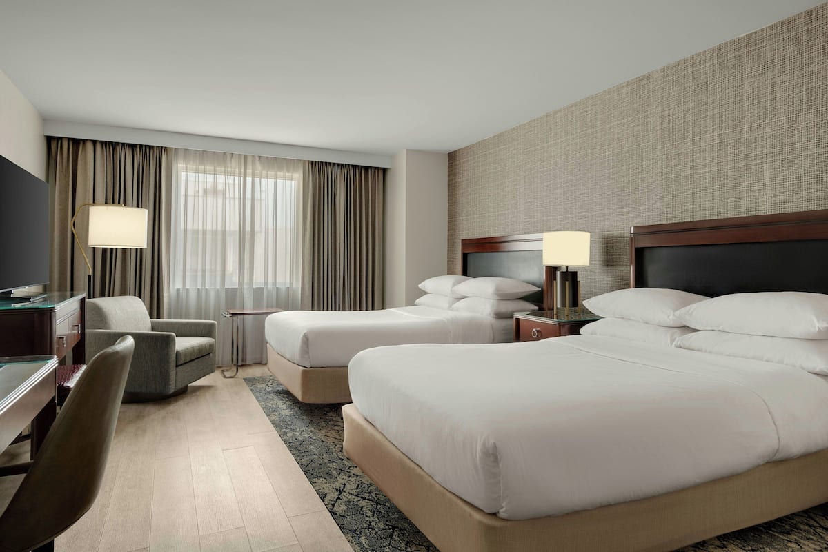 Une chambre d’hôtel avec deux lits, un bureau, une chaise et un téléviseur.