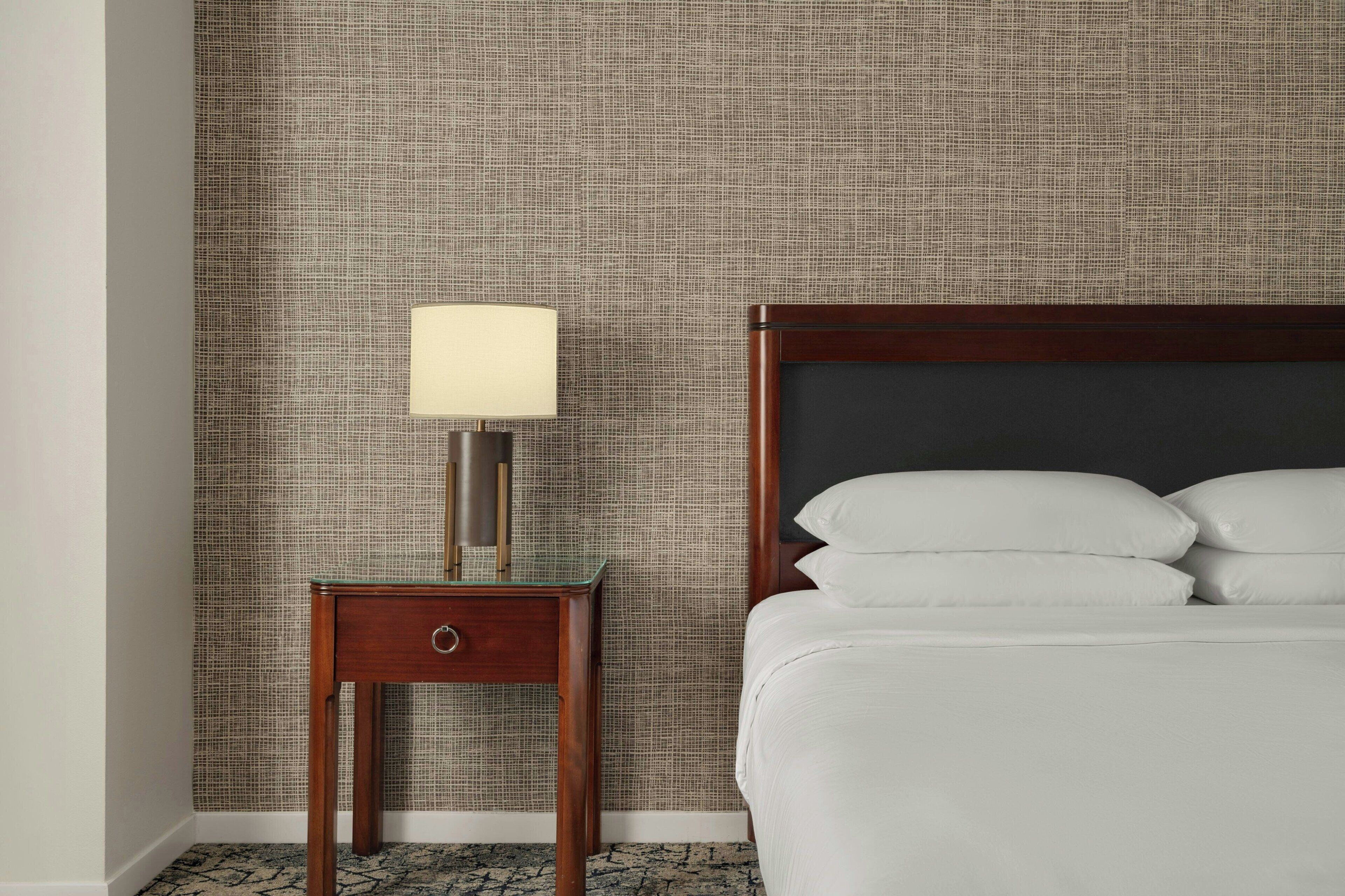 Een hotelkamer met een bed, een nachtkastje met een lamp en een gestructureerde muur.