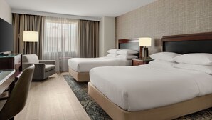 Habitación de hotel con dos camas, un escritorio, una silla, un televisor y una ventana con cortinas.