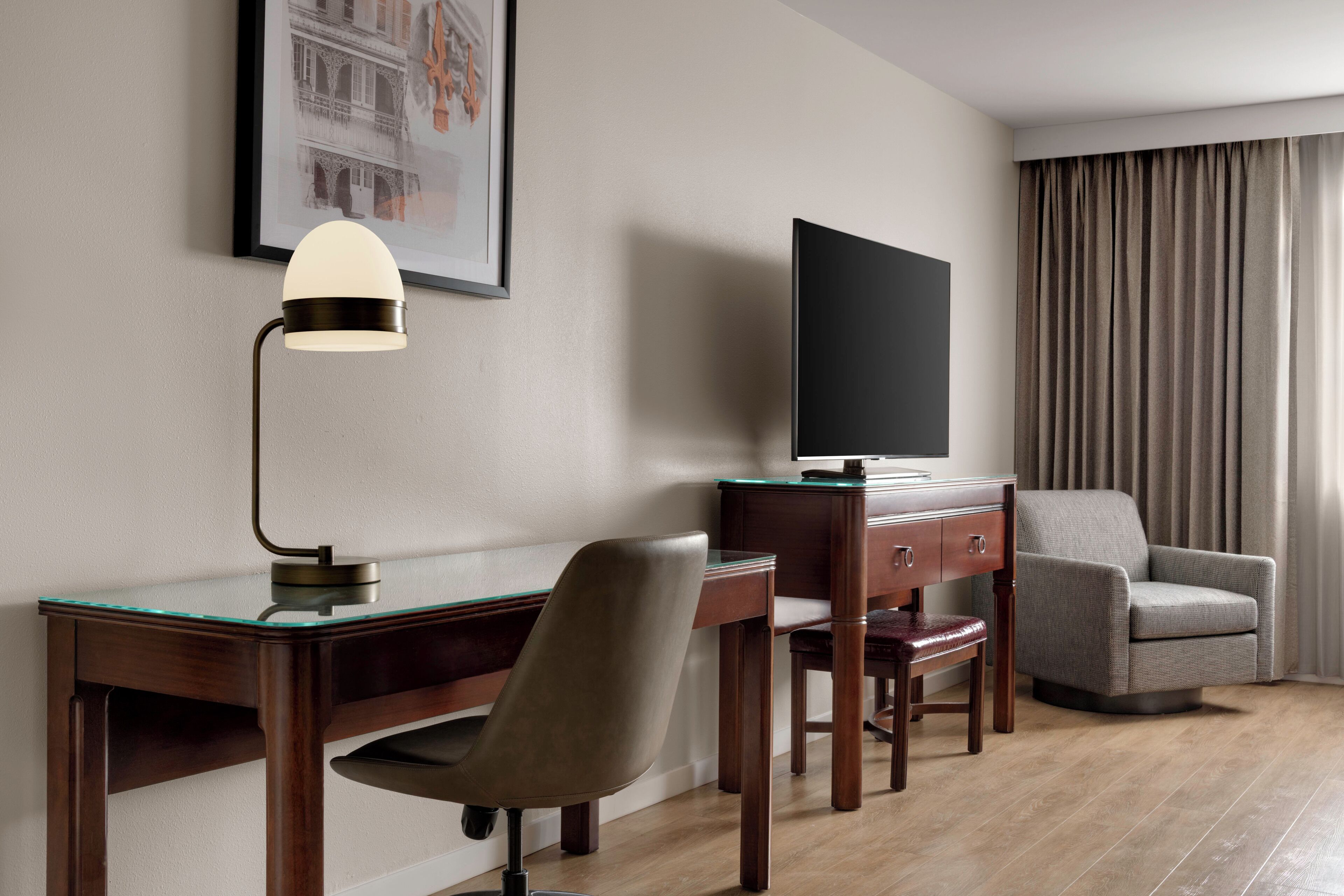 A hotel room with a desk, chair, television, and a sofa.