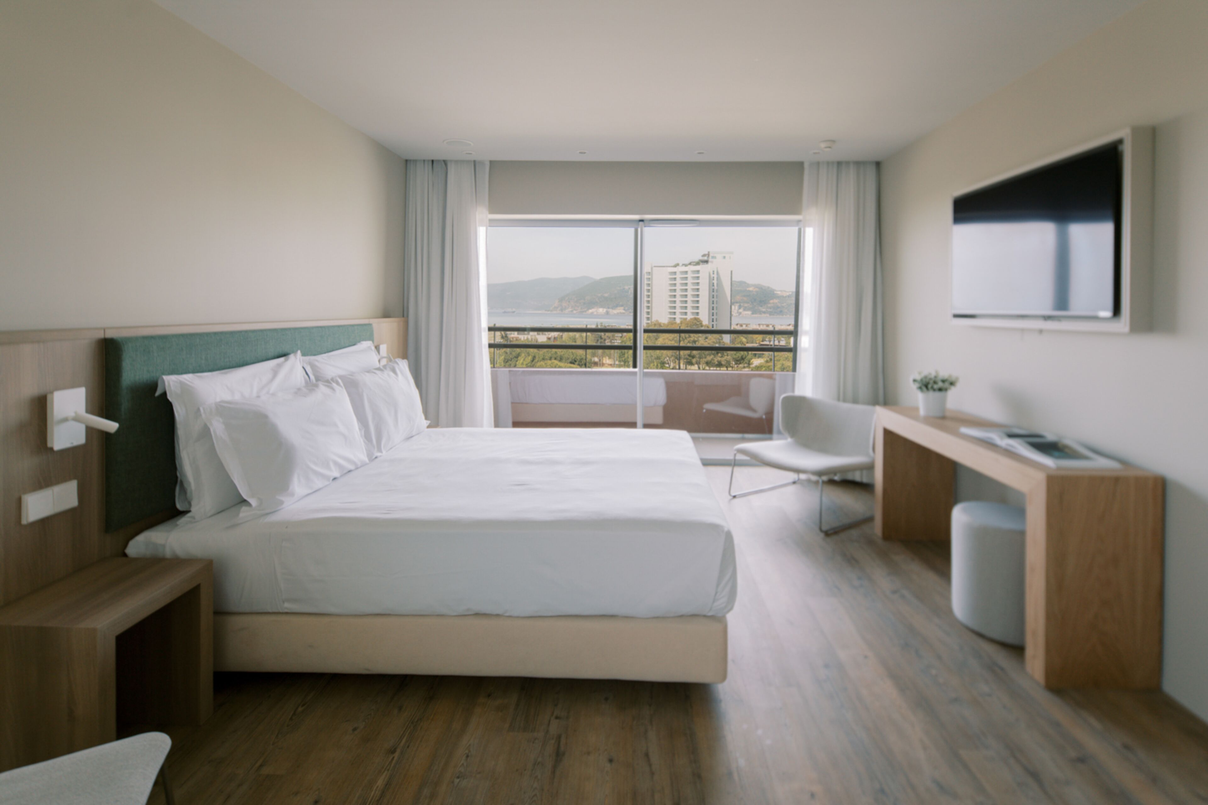 A modern hotel room with a large bed, a desk, a chair, and a TV.