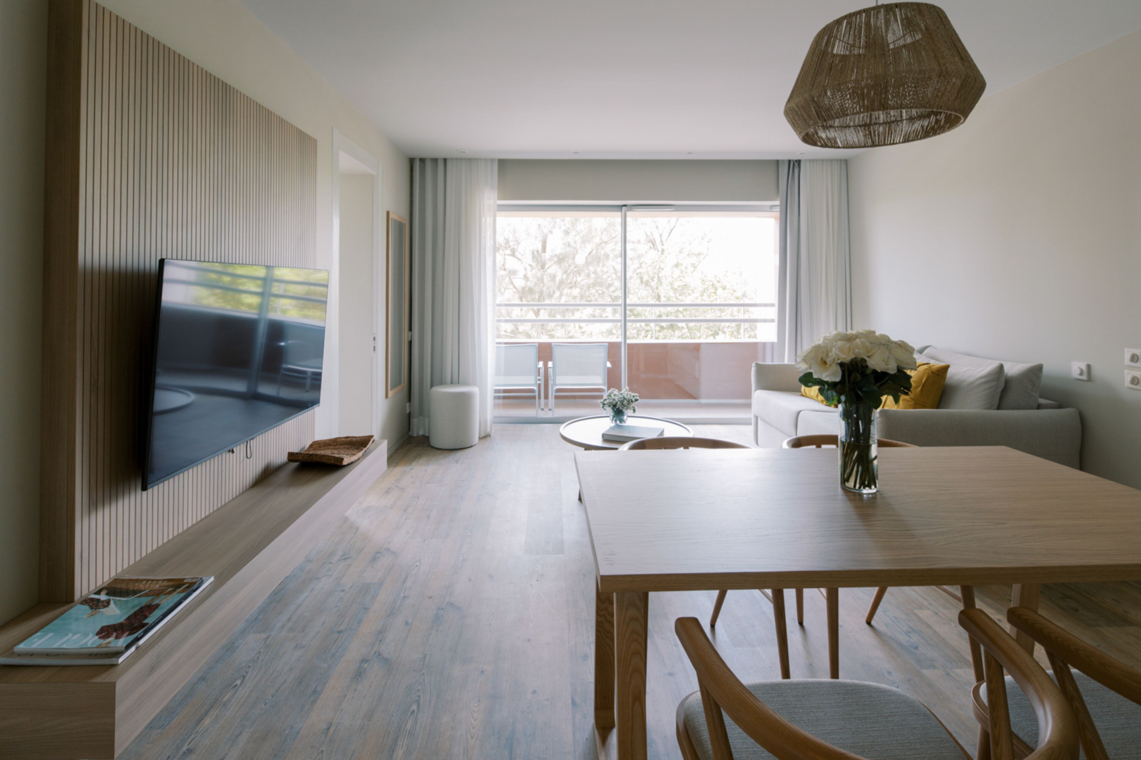 Una sala de estar moderna con un televisor de pantalla plana, una mesa de comedor de madera y un sofá con un jarrón de flores.