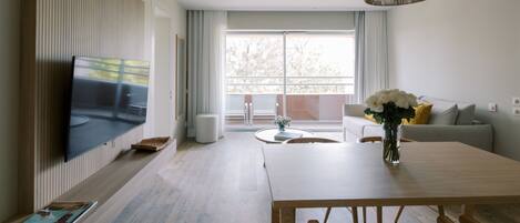 A modern living room with a flat-screen TV, a wooden dining table, and a sofa with a vase of flowers.