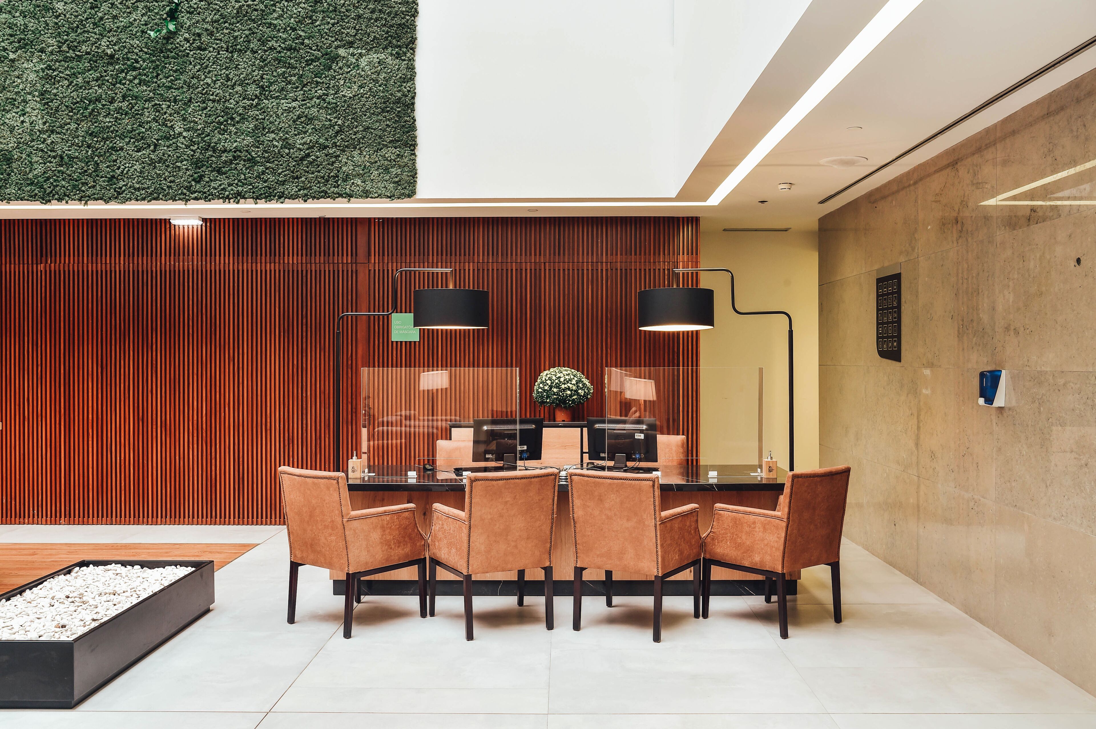 Een moderne receptiebalie met een wand van houten panelen, een glazen bureau en zes stoelen.