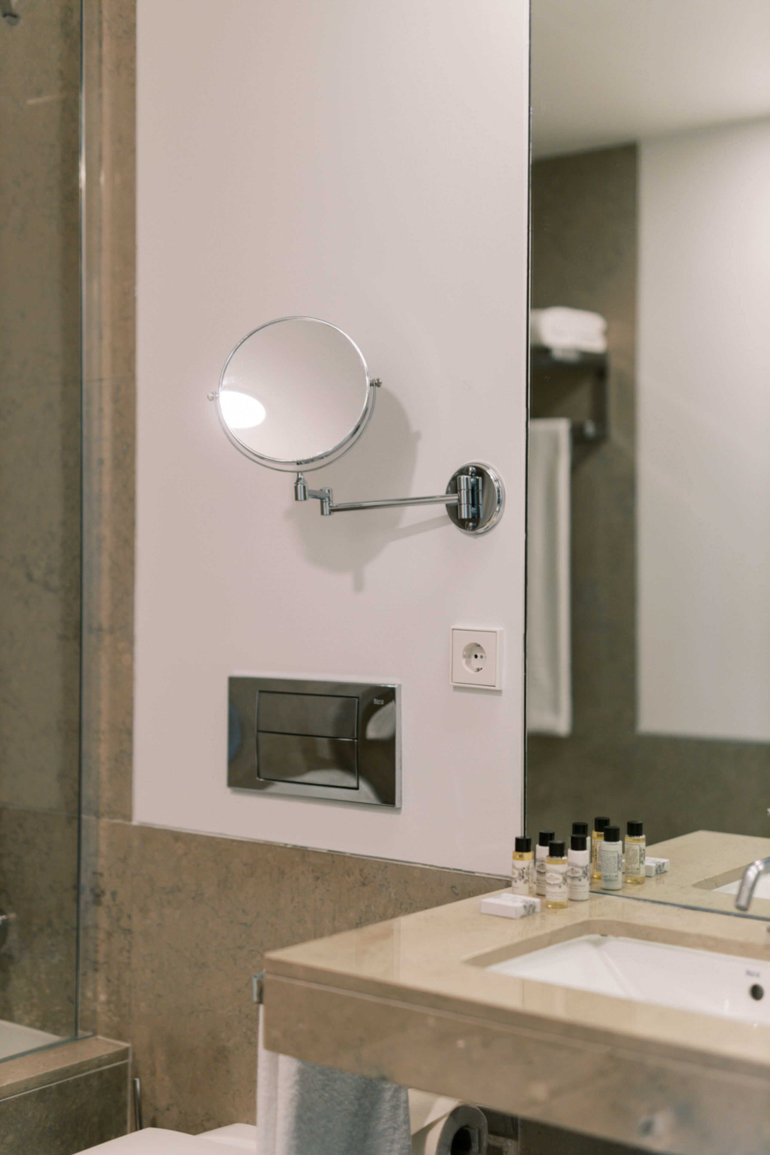 A bathroom with a round mirror, a sink, and toiletries on the counter.