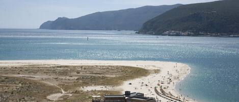 Na praia, areia branca, guarda-sóis, prática de vôlei de praia 