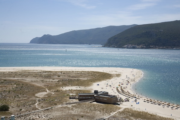 Na praia, areia branca, guarda-sóis, prática de vôlei de praia 