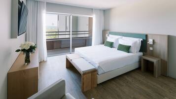 A modern hotel room with a large bed, a wooden bench, a bedside table, and a view of the outdoors.