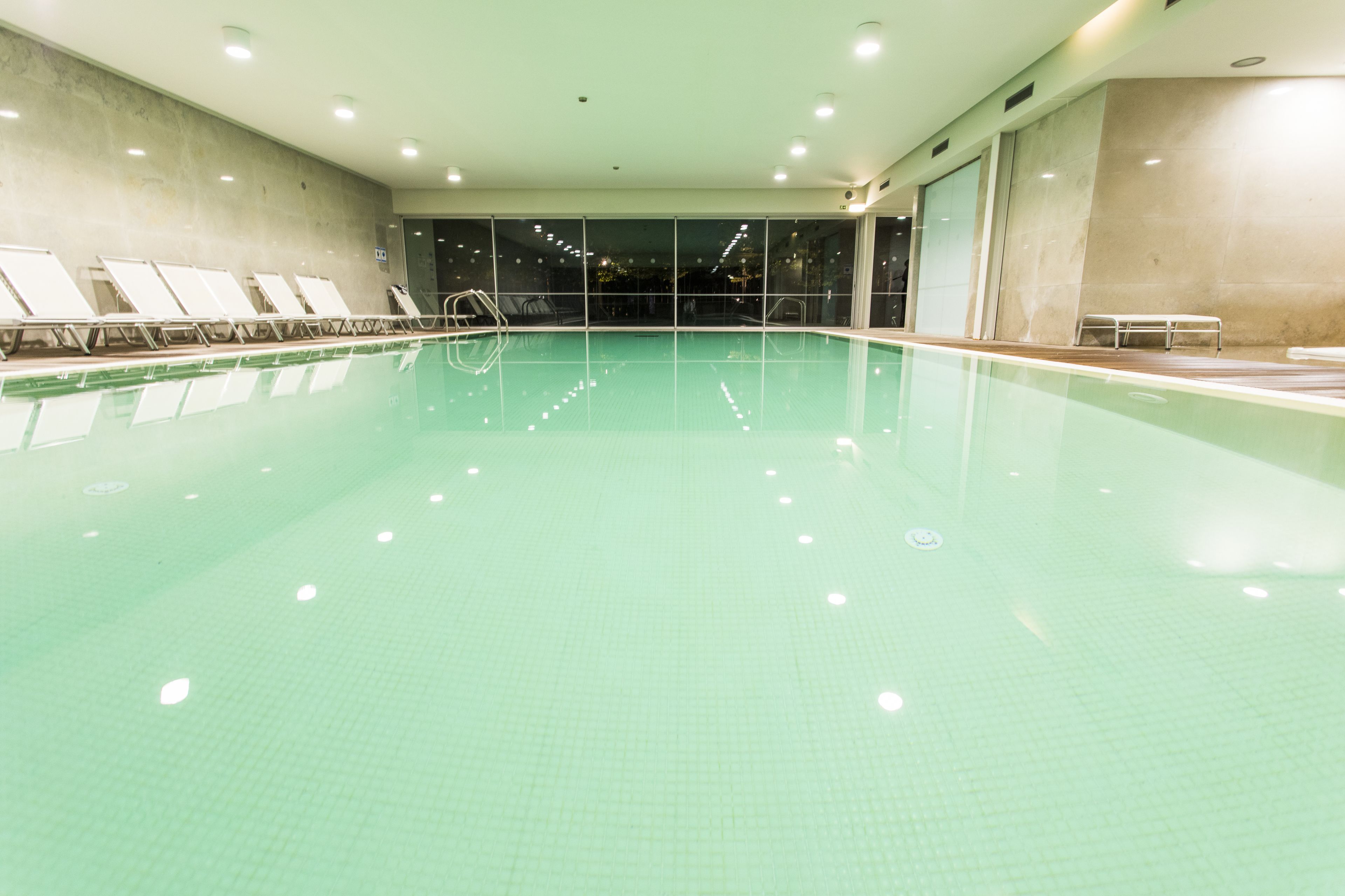 An indoor swimming pool with clear water, a tiled floor, and several lounge chairs along the side.