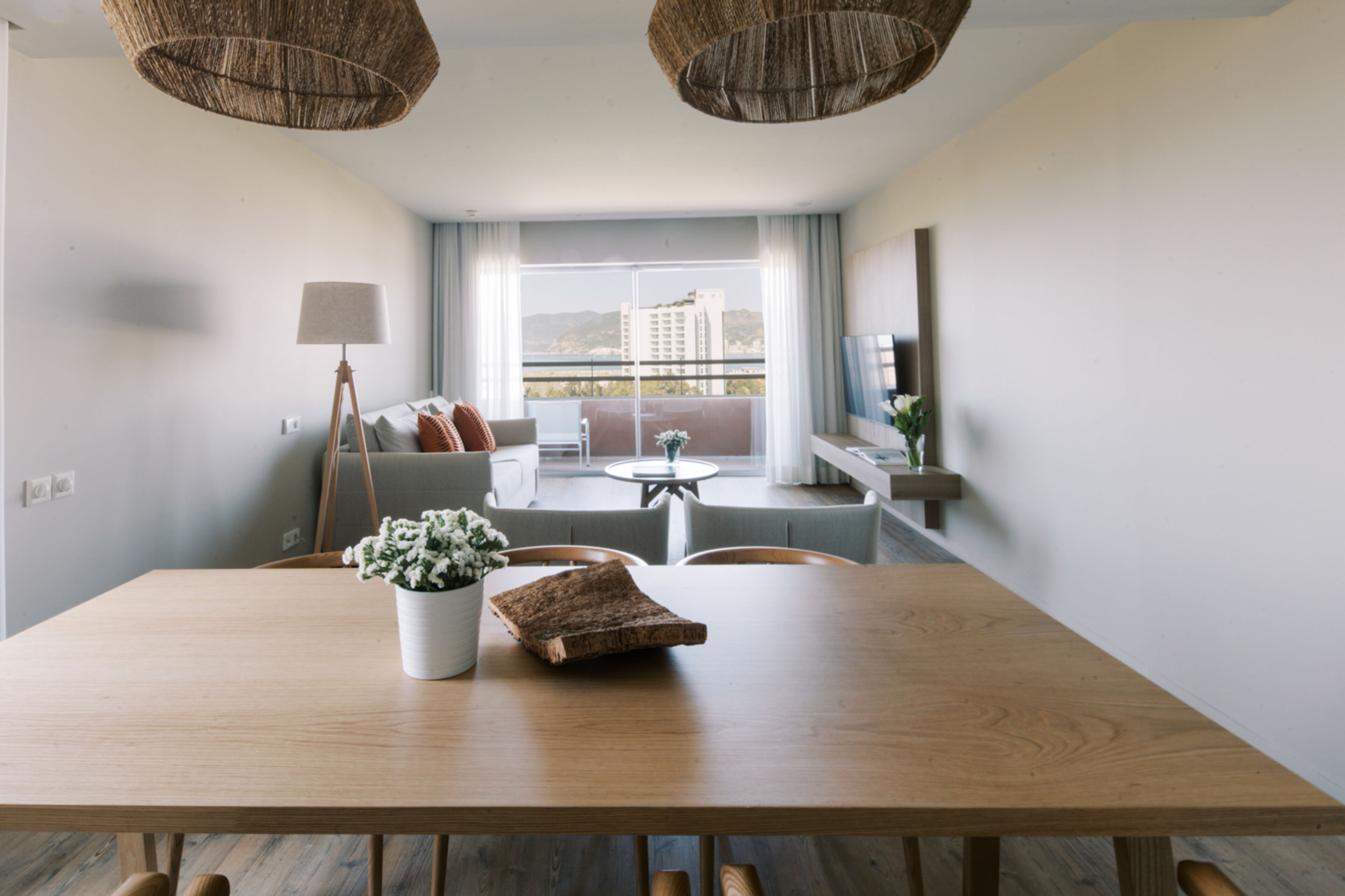 A modern living room with a wooden dining table, a sofa, and a balcony with a view.