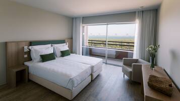 A modern hotel room with a large bed, a small desk, and a balcony with a view of the landscape.