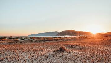 Eine Strandlandschaft mit Dünen und einem entfernten Berg bei Sonnenuntergang.