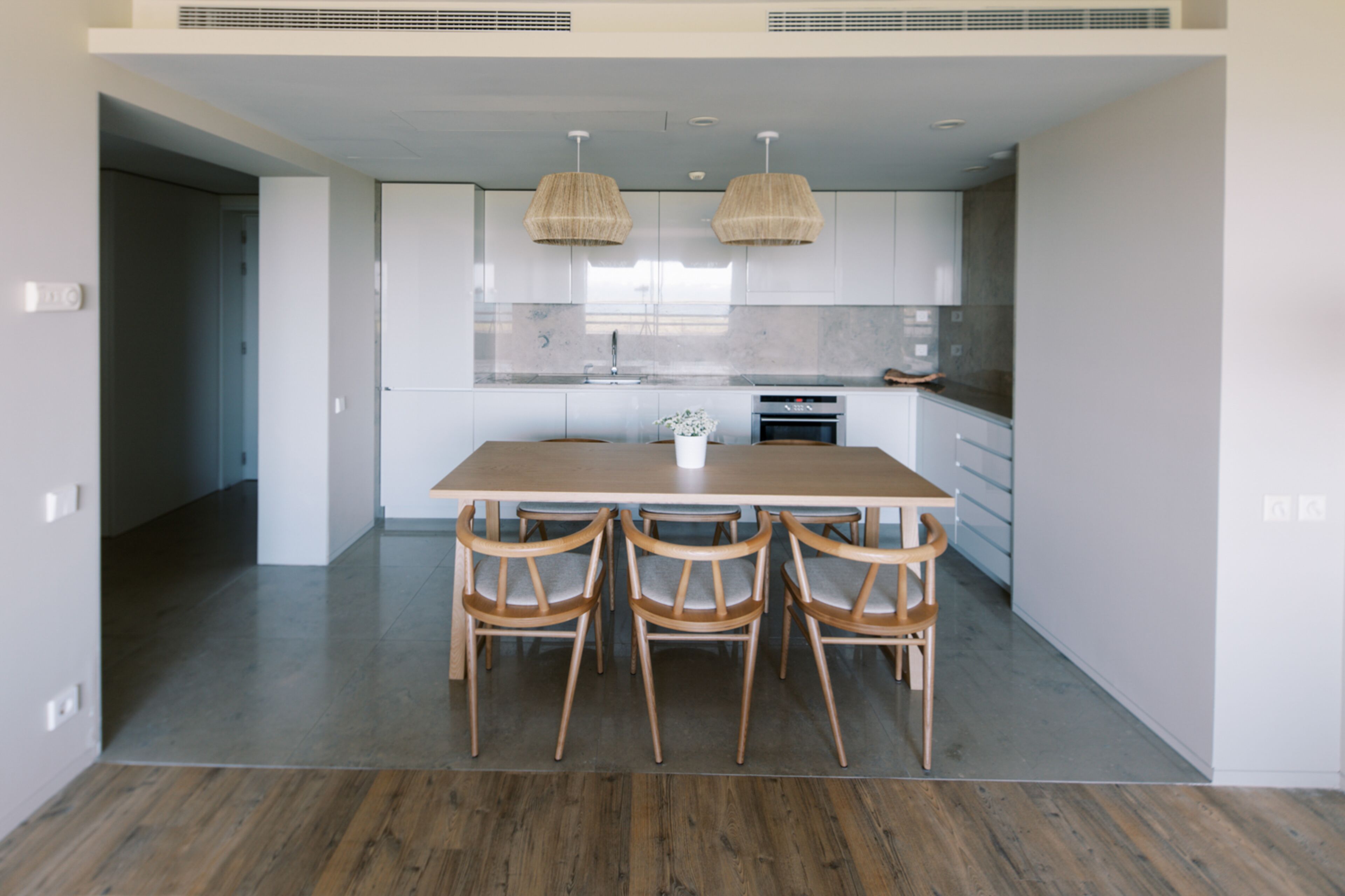 Una cocina moderna con armarios blancos, una mesa de comedor de madera y cuatro sillas.
