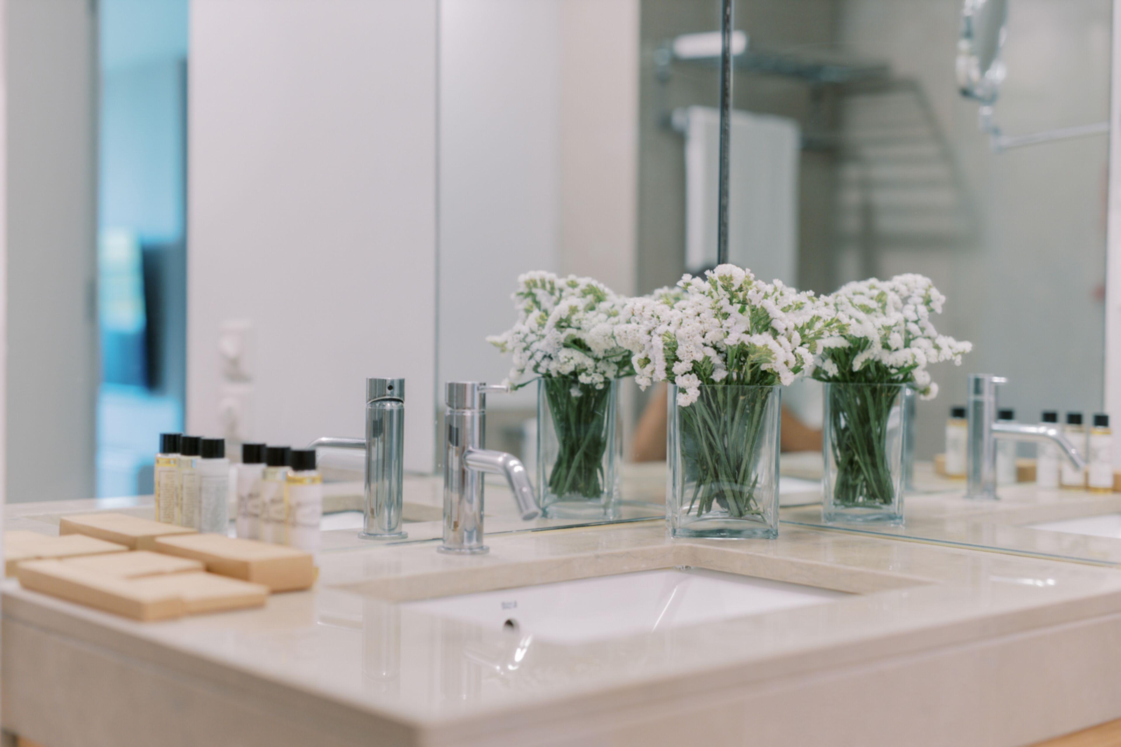 A bathroom with a white sink, two glass vases with white flowers, and various toiletries on the counter.