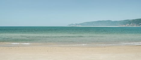 Une plage à l’eau claire, avec un rivage sablonneux et des montagnes qui se dessinent à l’horizon.