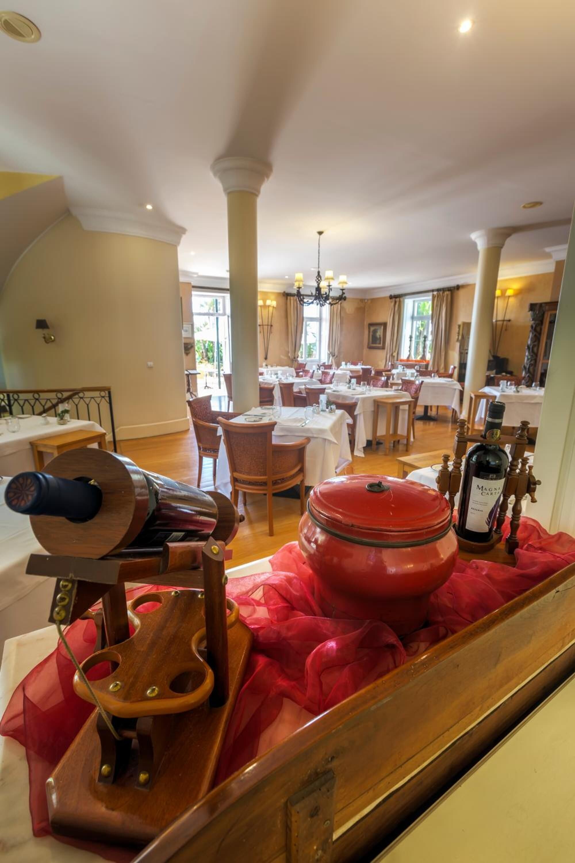 A dining area with tables set for service, a large red pot, and a wooden barrel.