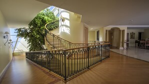 Un interior espacioso con suelo de madera, una escalera de caracol con baranda negra y un gran árbol al fondo.