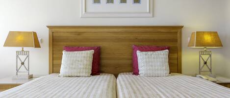 A double bed with striped bedding and two pillows, a wooden headboard, and a framed artwork above.
