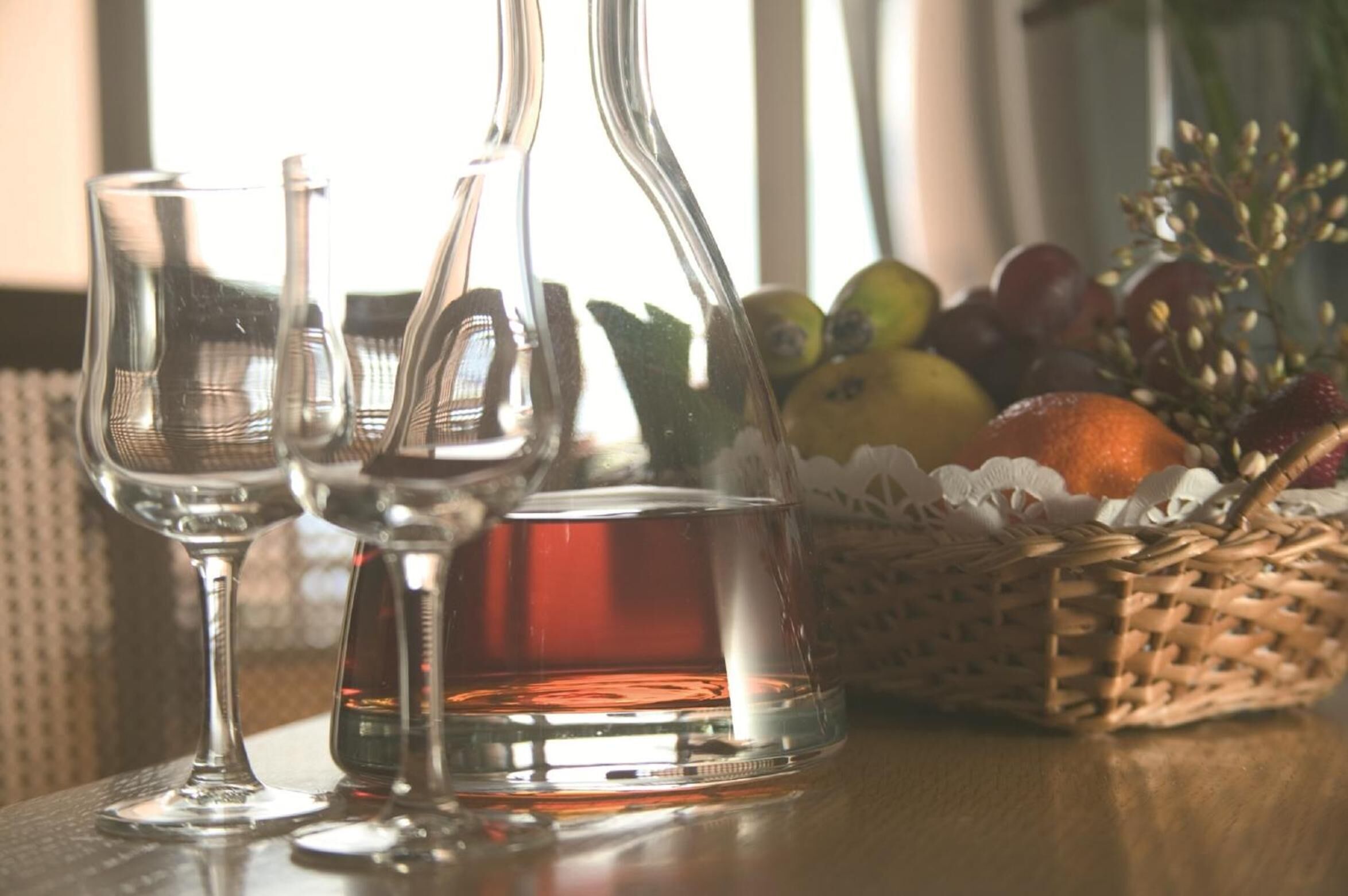 Une table avec une carafe en verre, deux verres à vin et un panier de fruits.