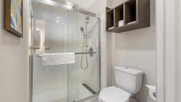 A modern bathroom with a glass-enclosed shower, a white toilet, and a small shelf above the toilet.