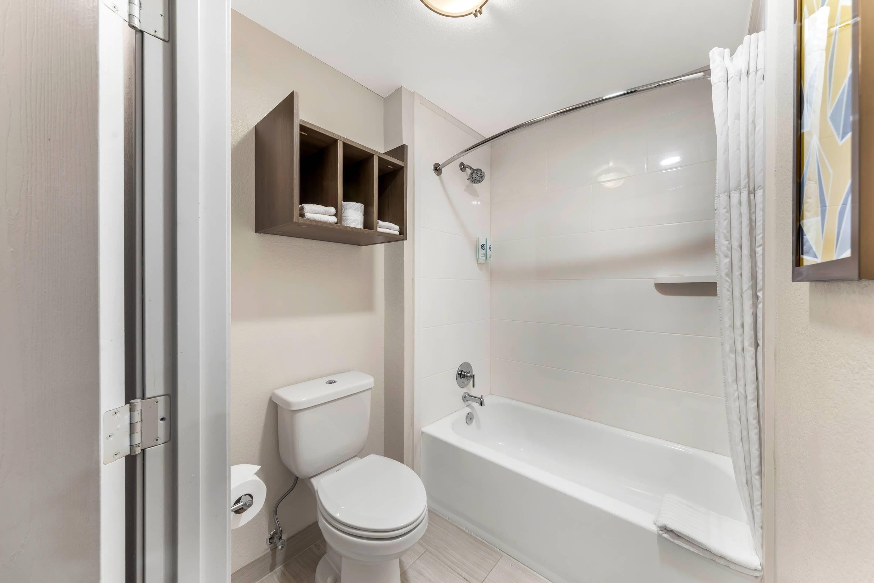 A bathroom with a toilet, a bathtub, and a shelf with towels.
