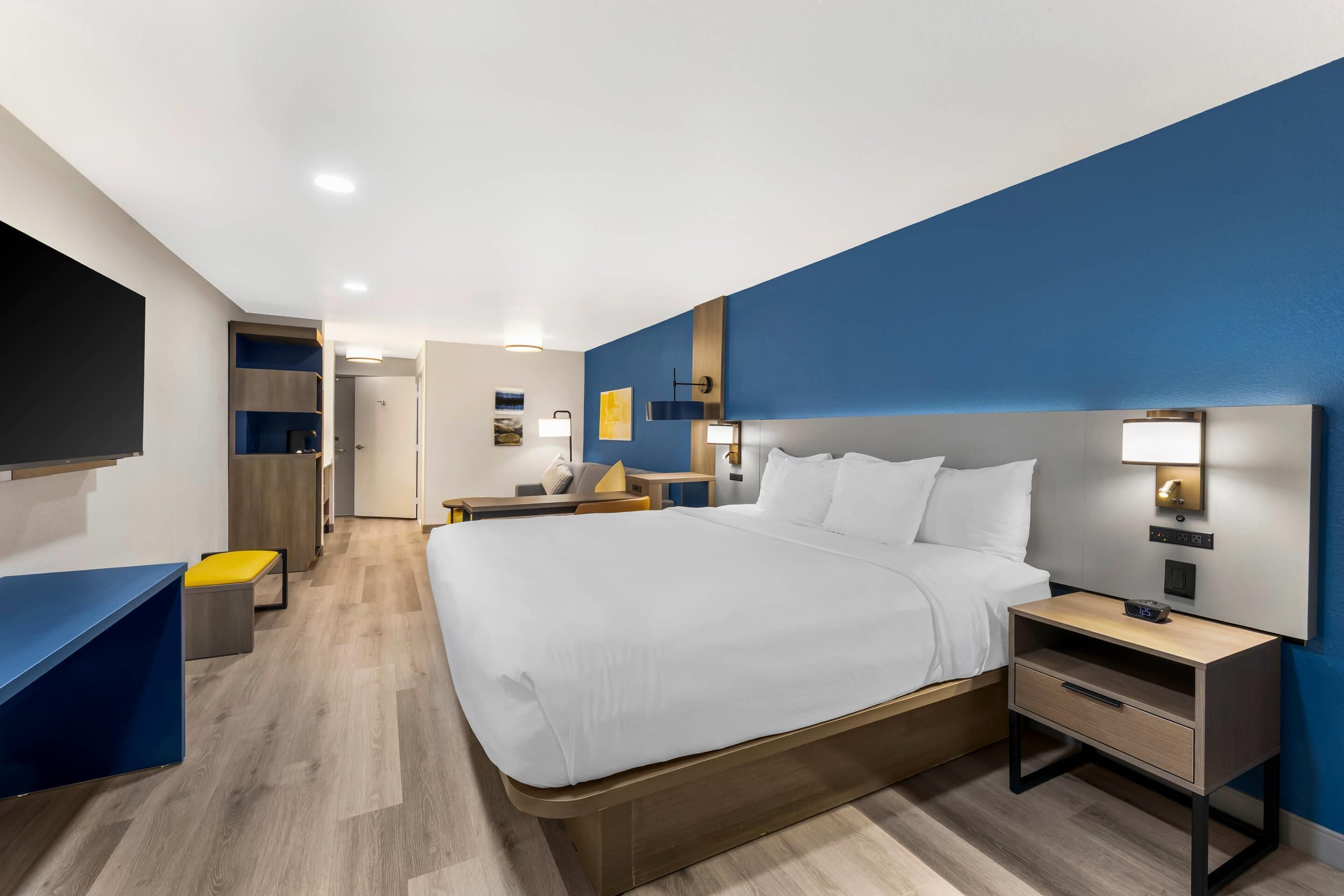 A modern hotel room with a large bed, bedside tables, a desk, and a TV.