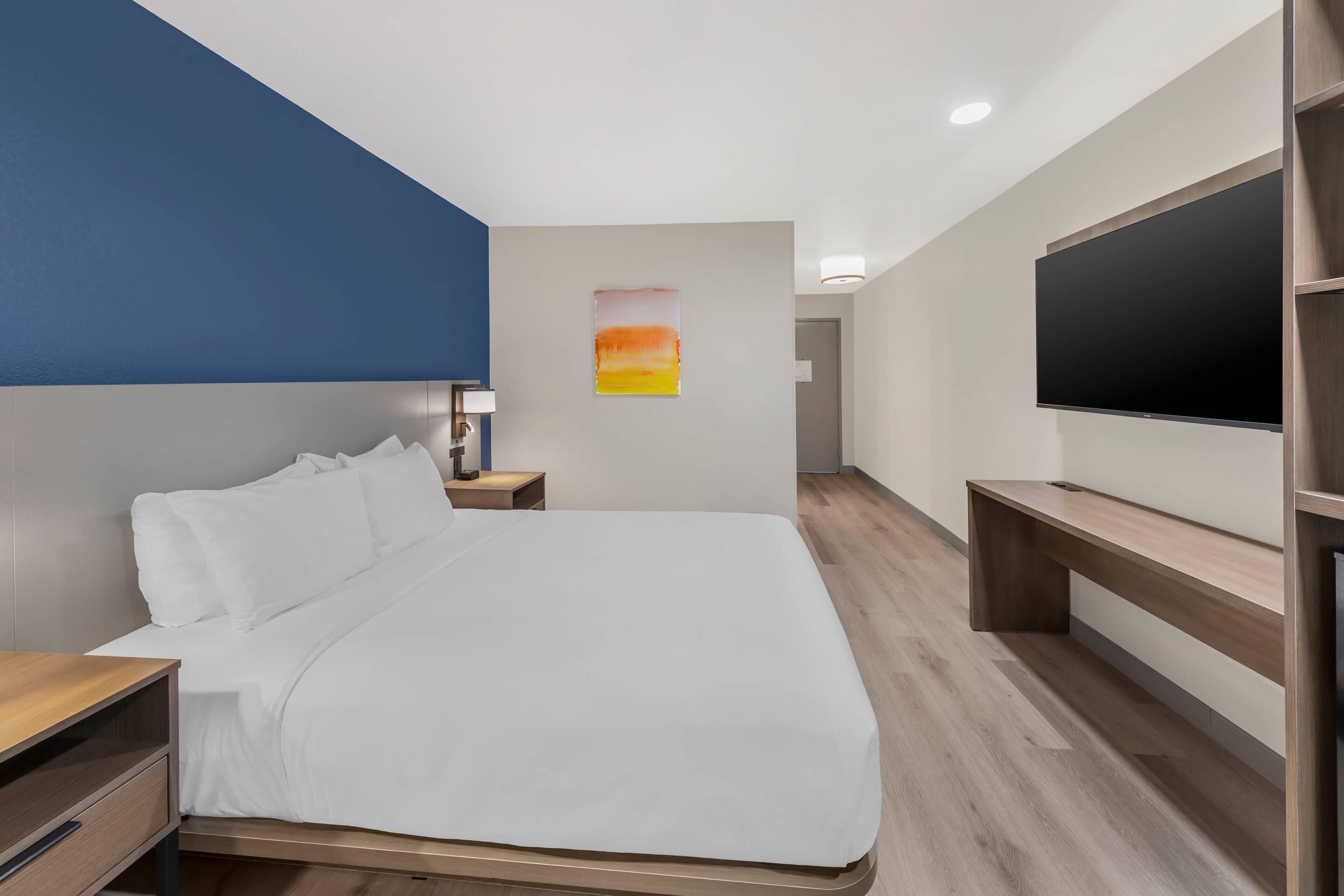 Una habitación de hotel moderna con cama, mesita de noche, lámpara, una obra de arte y televisión.